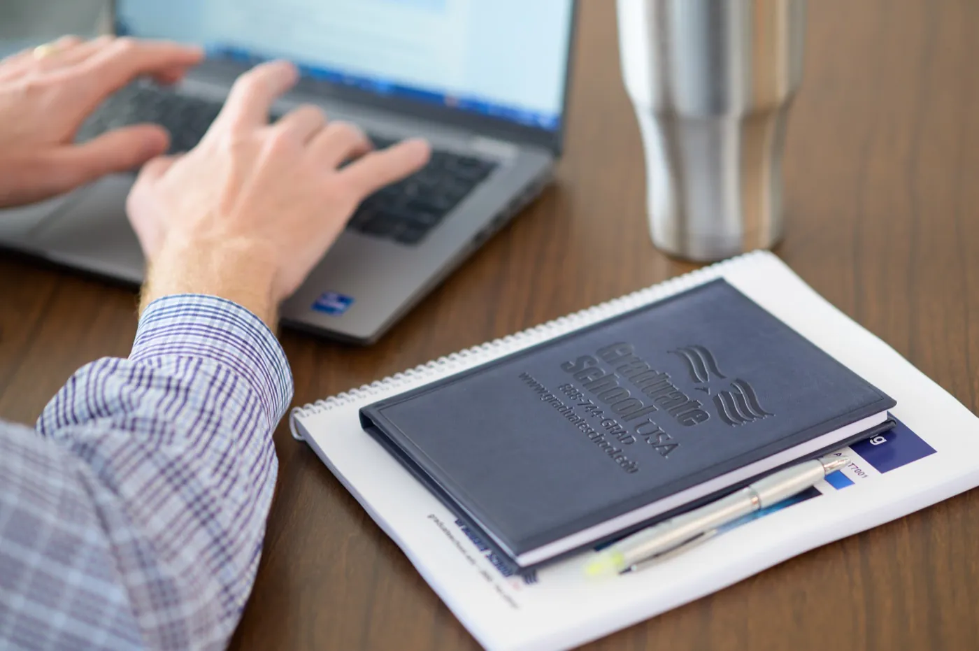A learner working on a laptop beside Graduate School USA course materials